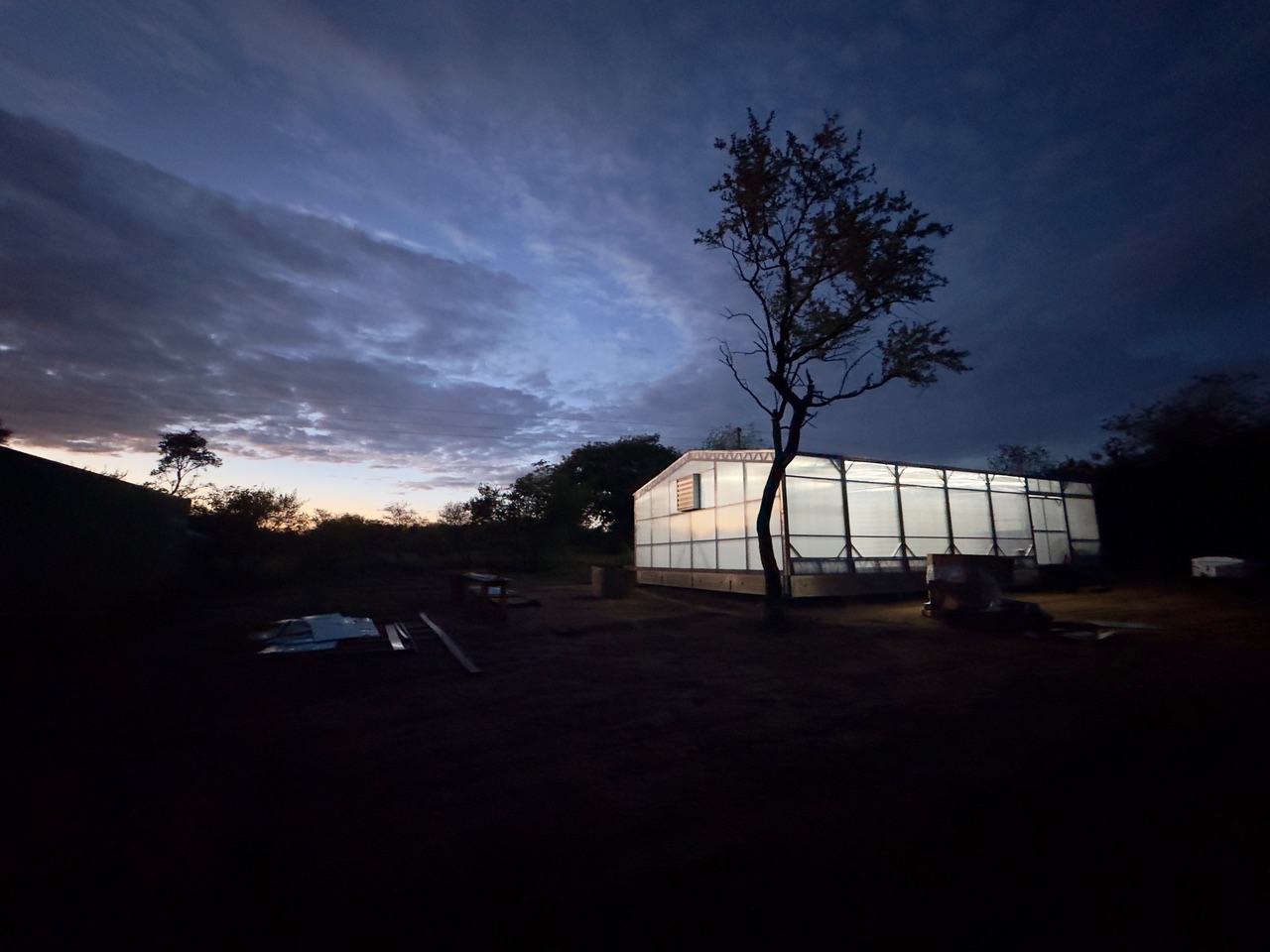 A FreshMinistries aquaponics greenhouse lit from within at dusk